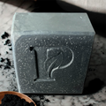 Prudent Preservations charcoal bar soap with embossed leaf logo, speckled texture, and minimalist design.
