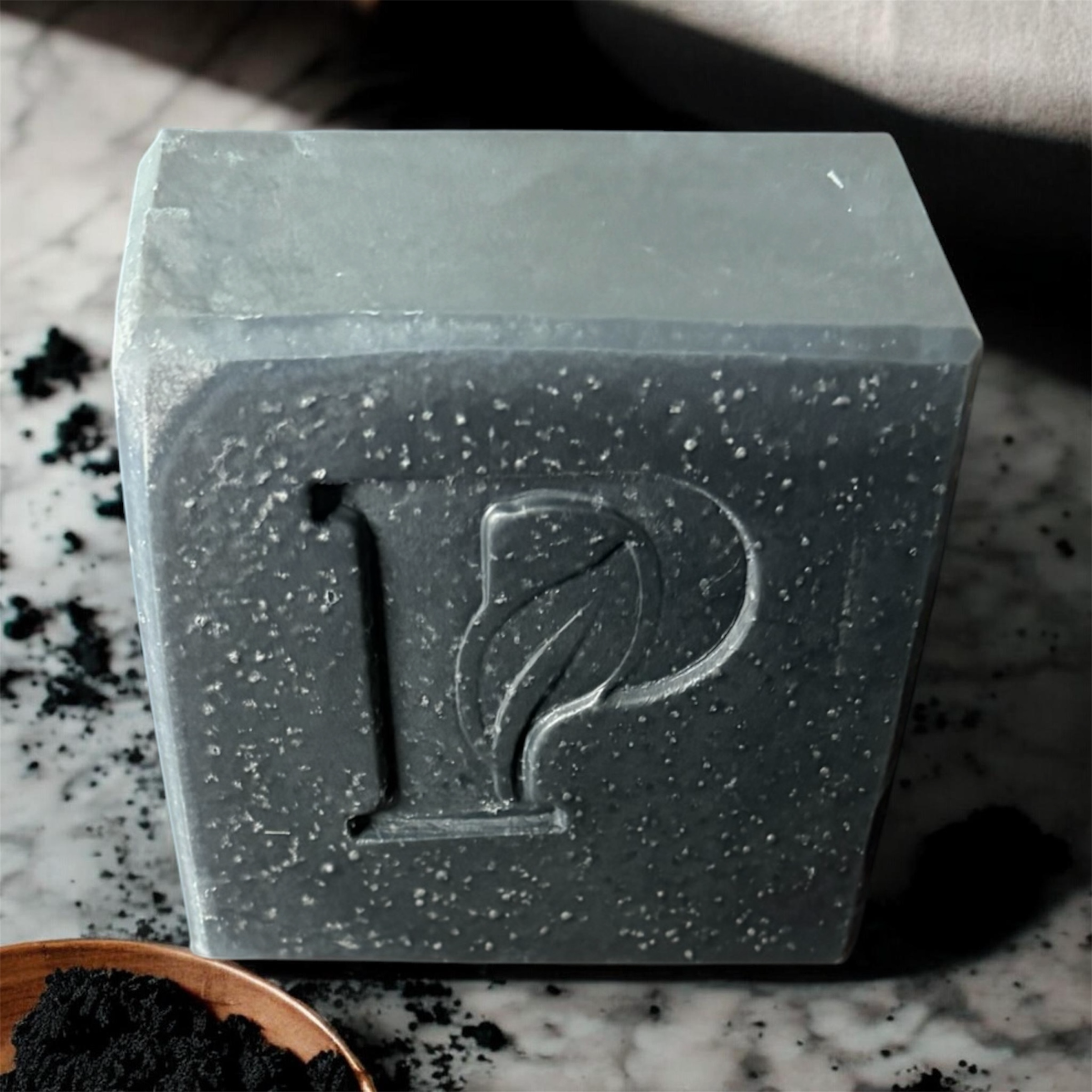 Prudent Preservations charcoal bar soap with embossed leaf logo, speckled texture, and minimalist design.